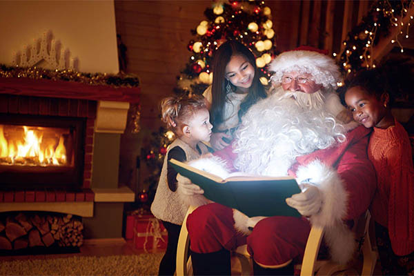 Duas crianças ao lado do papai noel lendo um livro com a magia do natal 2023